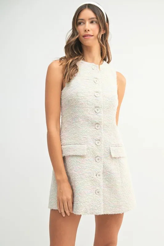 Model wearing sleeveless cream tweed mini dress with front buttons and flap pocket detail