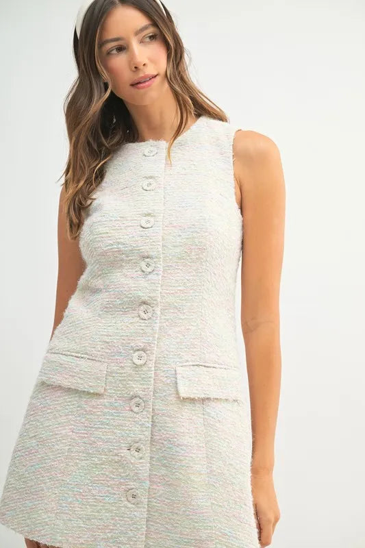 Close-up of cream textured tweed fabric and tonal buttons on structured mini dress