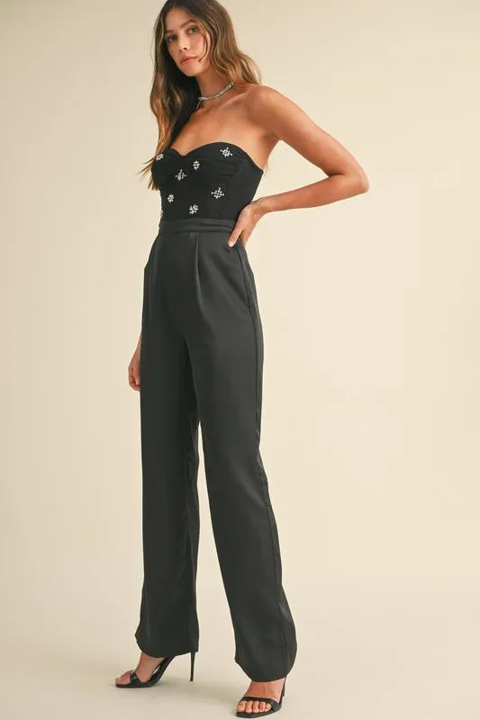 Side angle of black strapless jumpsuit with decorative rhinestones and tailored leg

